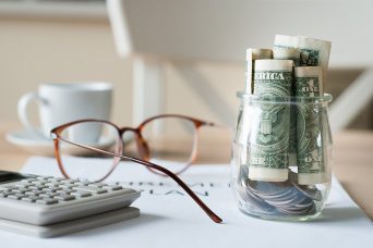 Calculating bills with calculator, glasses and money in a jar