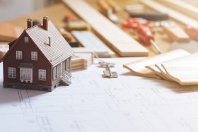 Homeownerl house model on a desktop with building materials and a blueprint design