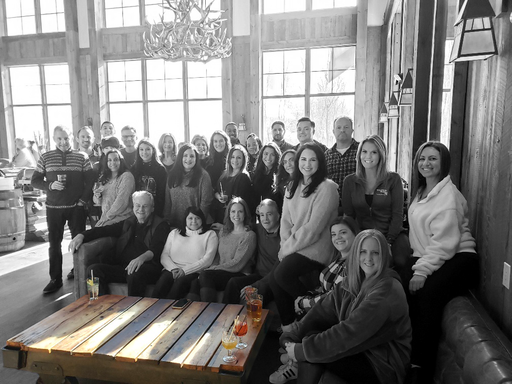 Group shot of Hanson & Ryan team sitting on a sofa in black and white with table in color