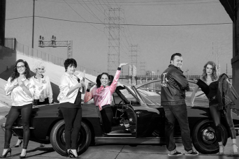 Team members dressed in 1950s attire pose in front of a classic car