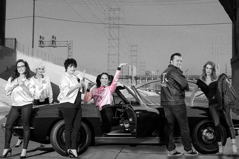 Team members dressed in 1950s attire pose in front of a classic car